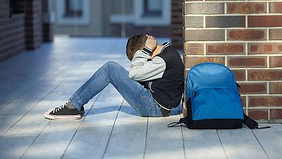 Un niño víctima de acoso escolar, sentado en el suelo del colegio