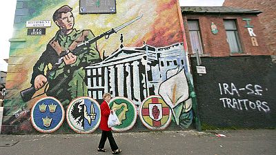 Una mujer pasa ante un mural nacionalista en Belfast, junto a una pintada que califica de "traidores" al IRA y al Sinn Féin Una mujer pasa ante un mural nacionalista en Belfast, junto a una pintada que califica de "traidores" al IRA y al Sinn Féin