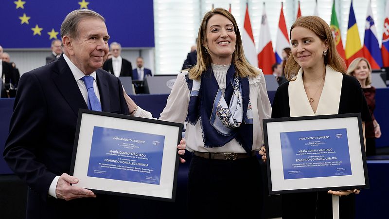 Ceremonia de entrega de premios: tres personas con certificados del Parlamento Europeo.  Banderas europeas al fondo.