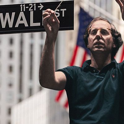 Gilbert Kaplan, con gafas y polo oscuro, dirige una orquesta imaginaria en Wall Street, Nueva York.  Imagen relacionada con Radio Clásica.