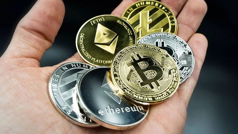 Mano sujetando diversas criptomonedas con detalles visibles como símbolos e inscripciones parciales en monedas de Bitcoin, Ethereum y Litecoin, entre otras.