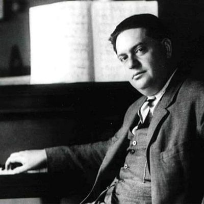 Retrato clásico en blanco y negro de un hombre en traje y corbata sentado al piano, con una mano sobre las teclas.