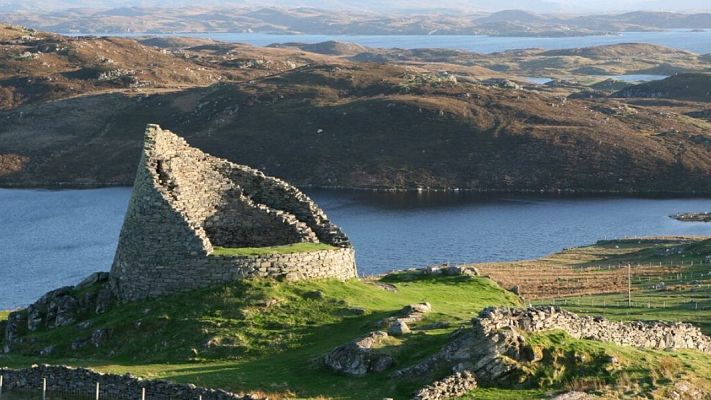 Ruinas cónicas de piedra junto a un lago en un paisaje montañoso. Atmósfera tranquila y evocadora.