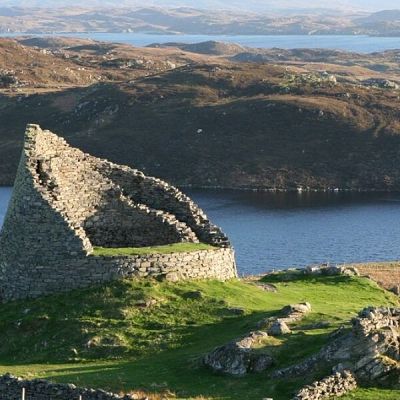 Ruinas cónicas de piedra junto a un lago en un paisaje montañoso. Atmósfera tranquila y evocadora.