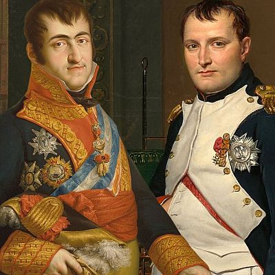 Dos hombres en uniformes militares, uno con chaleco blanco, posan en un interior con lámparas y reloj.  Uniformes con detalles dorados y bandas rojas.
