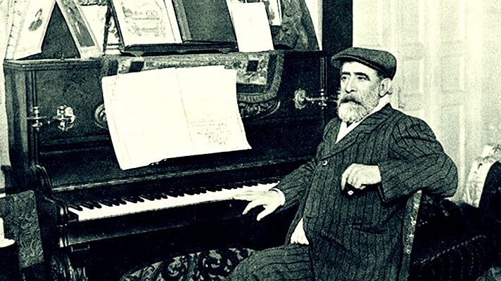 Tomás Bretón, compositor español, sentado al piano con partituras.  Viste traje a rayas y gorra; la imagen es en blanco y negro.