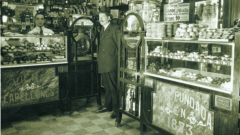 Interior de la pastelería VIENA CAPELLANES, fundada en 1873. Hombres posan tras mostradores con dulces. "VIENA CAPELLANES", "CASA FUNDADA EN 1873", "toda clase de pastelería", "DESDE 10 PESETAS".