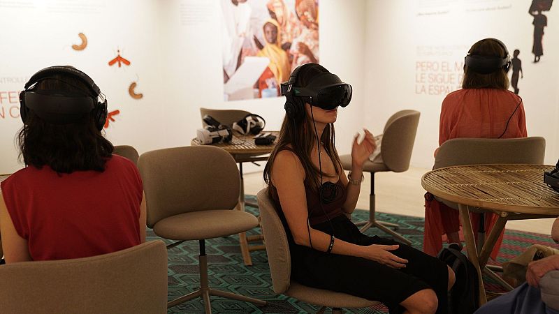 Personas experimentan realidad virtual en una sala de exposición moderna, con visores negros y auriculares, sentadas en sillas contemporáneas.