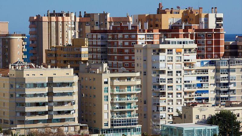 Una vista de numerosos edificios residenciales de diferentes alturas y estilos arquitectónicos, con balcones y ventanas variadas, creando un paisaje urbano bajo un cielo despejado. Se observa vegetación en la parte inferior de la imagen.