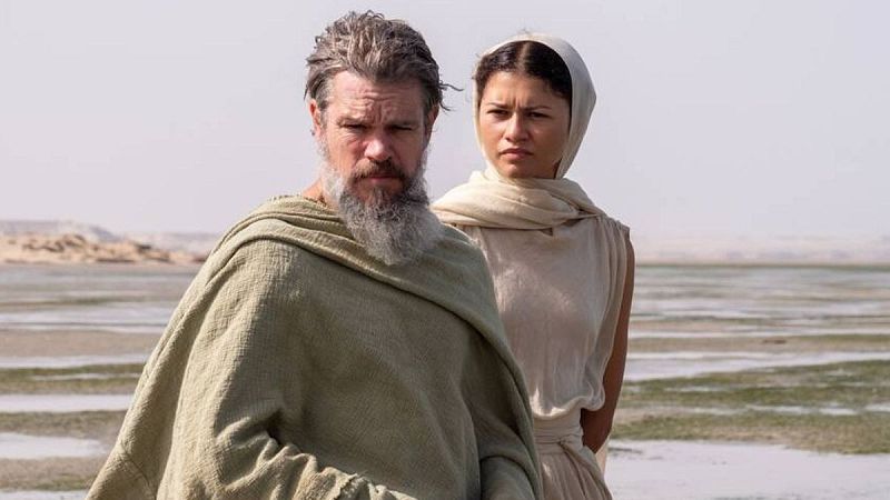 Christian Bale y Zendaya posan en un paisaje árido, él con barba canosa y túnica verde, ella con pañuelo crema. La escena es cinematográfica y desolada.