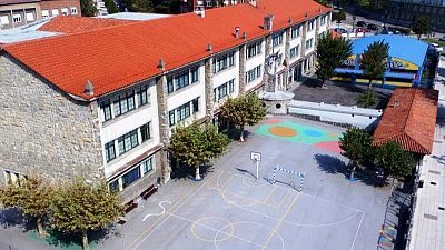 Vista a�rea de un complejo escolar con edificio principal, patio con canchas deportivas, zonas de juego y �rboles. Se aprecian edificios adyacentes y entorno urbano.