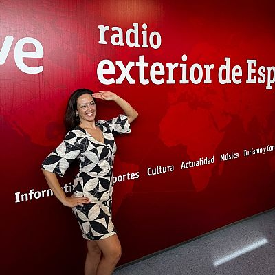 Clara Irazábal sonríe a la cámara con un vestido geométrico, frente a un fondo rojo con \"rtve\" y \"radio exterior de España\".