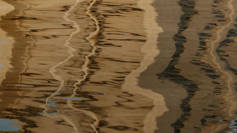 Reflejos abstractos en agua con tonos c�lidos y oscuros, l�neas onduladas y fluidas que crean un patr�n din�mico y una sensaci�n de profundidad.