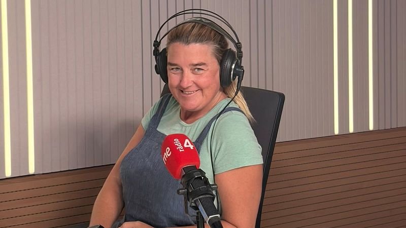 Imma Sust, periodista espa�ola, en estudio de radio con micr�fono RNE Radio 4, auriculares negros, camiseta verde menta y peto vaquero. Fondo con paneles grises y luces c�lidas.
