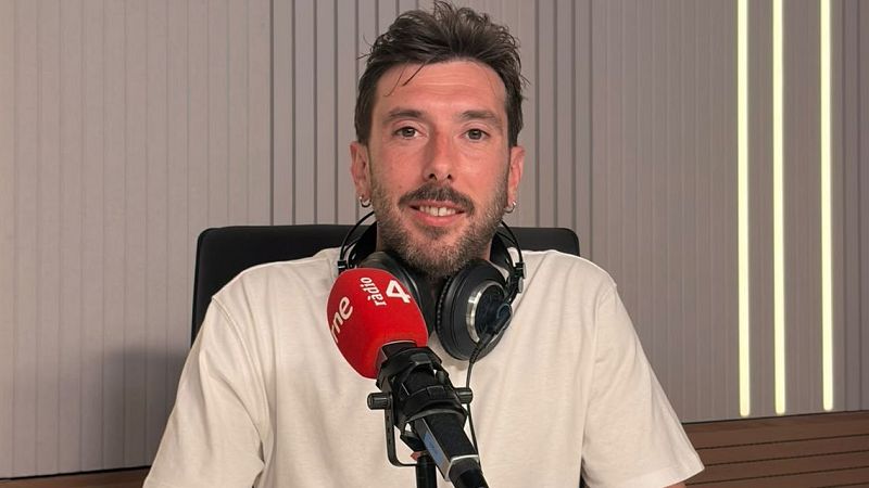 Marc Llibre, presentador de radio, en un estudio con micr�fono RNE R�dio 4. Lleva camiseta beige, auriculares y barba. Fondo con luces LED amarillas y paneles ac�sticos.