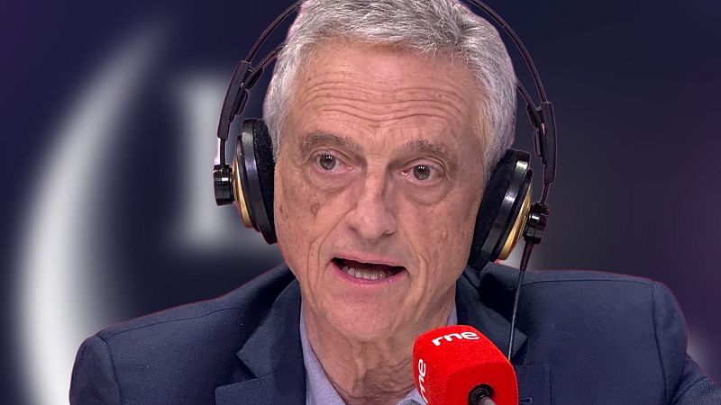 Luis Rojas Marcos, psiquiatra, en un estudio de RNE con auriculares y micrófono, vestido con traje azul oscuro. Fondo oscuro y desenfocado.