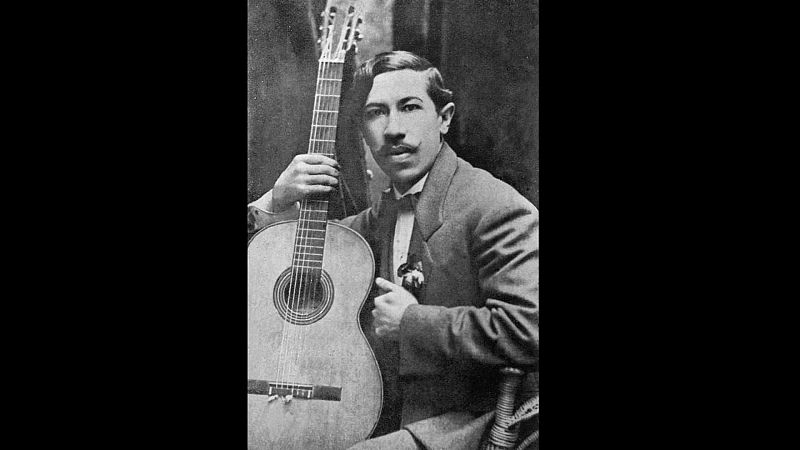Agust�n P�o Barrios 'Mangor�' en un retrato de 1910. Viste traje formal y sostiene una guitarra cl�sica, mirando fijamente a la c�mara con expresi�n serena. Fondo oscuro de estudio.