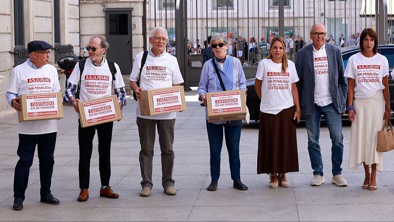 Manifestantes con camisetas blancas y cajas de cartón reivindican jubilación anticipada sin penalizar con más de 40 años cotizados frente a un edificio institucional.