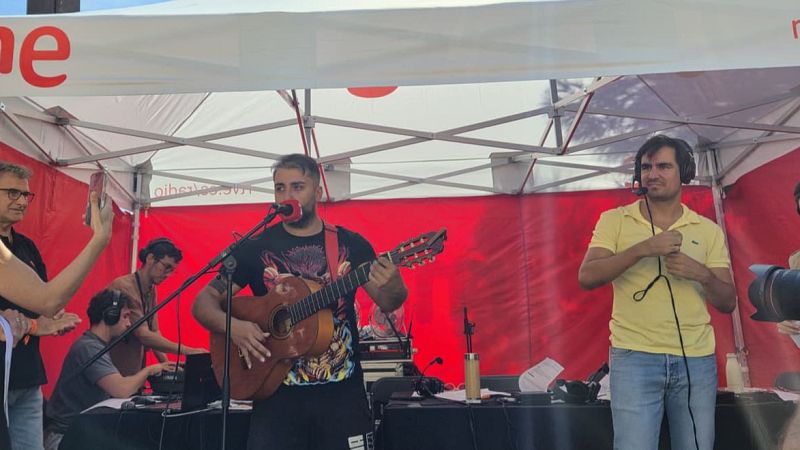 Dani Pubill canta y toca la guitarra bajo una carpa blanca con lona roja de fondo. Un hombre con auriculares y otro aplaudiendo completan la escena de una actuaci�n musical.