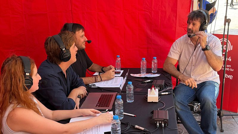 Cuatro personas participan en una emisi�n de radio, con Adam Mart�n a la derecha. Llevan auriculares y micr�fonos, y hay equipo de audio y botellas de agua sobre la mesa. El fondo muestra el logo "R�dio 4".
