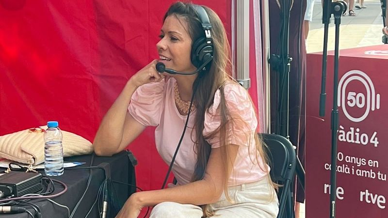 Claudia Mart�n, presentadora de R�dio 4, sonr�e durante una emisi�n, luciendo auriculares y micr�fono. El fondo muestra el logo de R�dio 4 y la celebraci�n de sus 50 a�os.