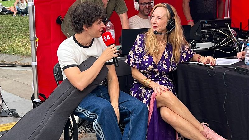 Roger Padr�s entrevista a Elisenda Roca en una retransmisi�n de radio al aire libre. Se aprecian equipo t�cnico, un toldo rojo y p�blico al fondo.