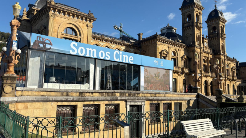 Ayuntamiento de San Sebastián con estructura moderna "Somos Cine" de rtve. Valla verde, banco blanco y farol clásico en primer plano. Cielo azul.