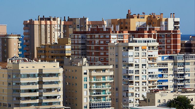 Vista panorámica de una densa ciudad costera con edificios residenciales de variadas alturas y colores, bajo un cielo azul y mar al fondo.