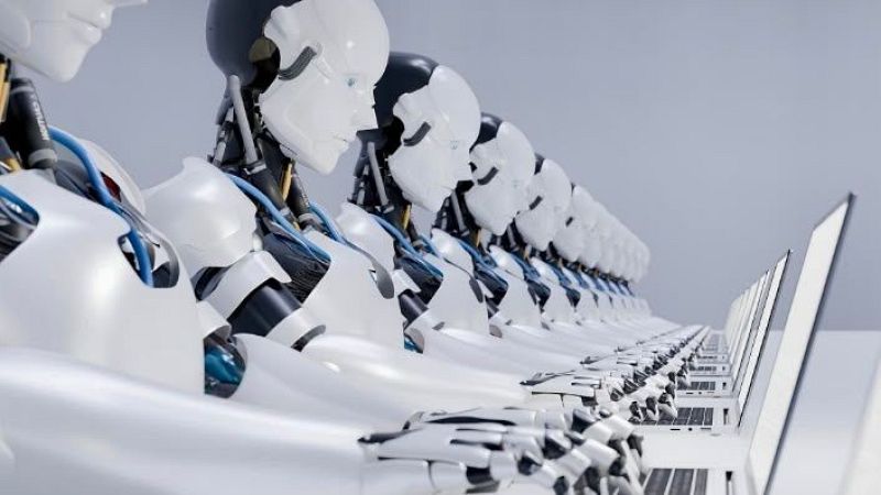 Robots humanoides id�nticos, con detalles tecnol�gicos visibles, interact�an con ordenadores port�tiles en una fila ordenada, evocando una visi�n de automatizaci�n avanzada.