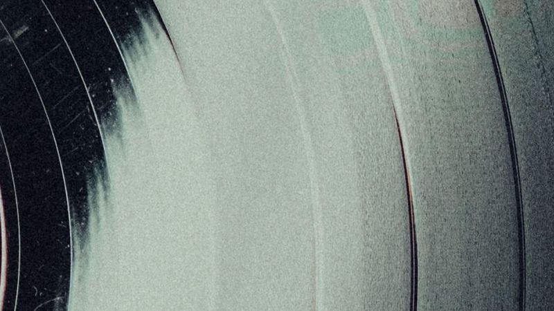 Superficie de disco de vinilo con surcos conc�ntricos en zona oscura y textura granulada en zona clara, dividida diagonalmente.