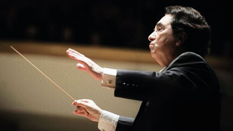 Primer plano de perfil de Enrique Garc�a Asensio, director de orquesta, dirigiendo con batuta y gesto expresivo. Fondo oscuro y desenfocado.