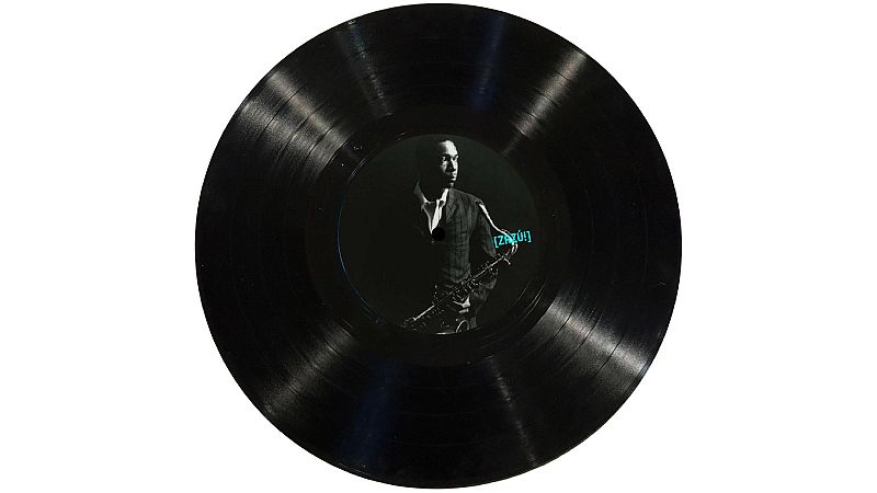 Disco de vinilo negro con John Coltrane de perfil y saxof�n en la etiqueta central. Texto azul "[ZAZ�!]" a la derecha.