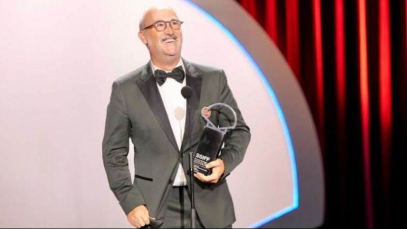 Javier C�mara, actor espa�ol, sonr�e en el escenario con un esmoquin y un premio "SSIFF" del Festival de San Sebasti�n. Un micr�fono a su lado.