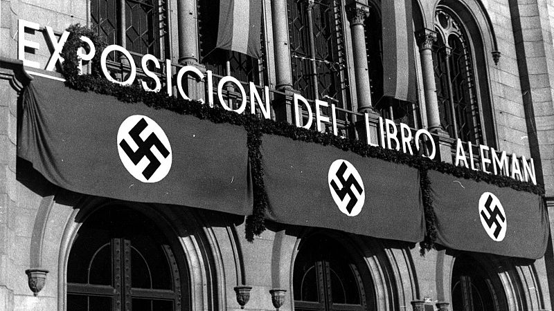 Fachada de edificio con letrero "EXPOSICION DEL LIBRO ALEMAN" y estandartes con esv�sticas. Decoraci�n con guirnaldas y posible bandera espa�ola. Evento de propaganda nazi en Barcelona.