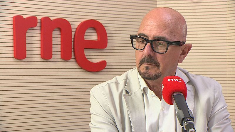 César Pascual, Consejero de Salud, en un estudio de RNE. Micrófono profesional con funda roja y logo de RNE en primer plano.
