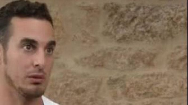 Primer plano de un hombre con pelo oscuro, barba y expresi�n de sorpresa, mirando a su izquierda. Fondo de pared de piedra.