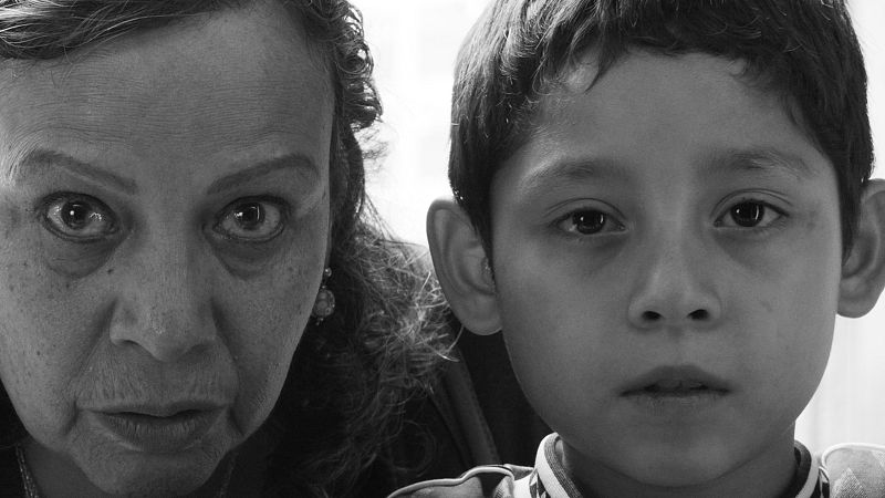Primer plano en blanco y negro de una mujer y un niño, sus rostros muy juntos, ambos mirando directamente al espectador con expresiones intensas.