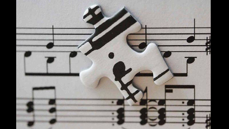 Pieza de puzle blanca con notaci�n musical negra sobre una partitura musical. Los s�mbolos de la pieza contin�an la partitura debajo.