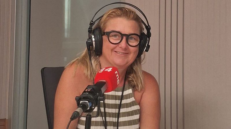 La periodista Imma Sust sonr�e en un estudio de radio frente a un micr�fono con el logo de "rne", vistiendo un top a rayas y gafas de montura negra.