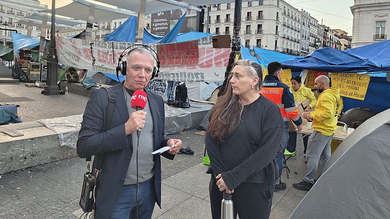 Un reportero de RNE entrevista a Gara en la Puerta del Sol de Madrid, frente a un campamento de protesta con una pancarta que dice "LA LUCHA DE HOY ES LA DIGNIDAD DEL MAÑANA".