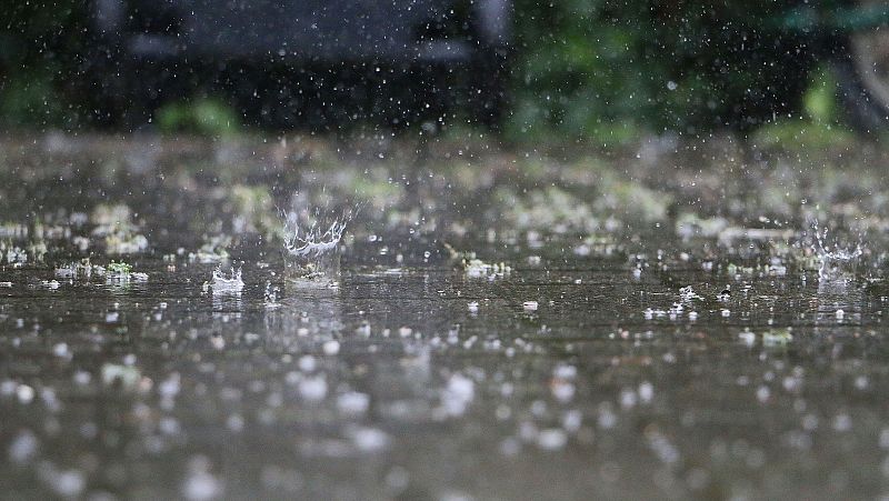 Primer plano de gotas de lluvia impactando sobre un suelo pavimentado y mojado, destacando una salpicadura en forma de corona de agua con un fondo oscuro y desenfocado.