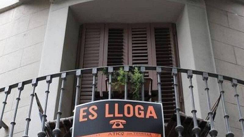 Balc�n de piedra con contraventanas cerradas y un cartel de alquiler que dice "ES LLOGA" y "�TICO con TERRAZA" colgado de su barandilla de hierro.