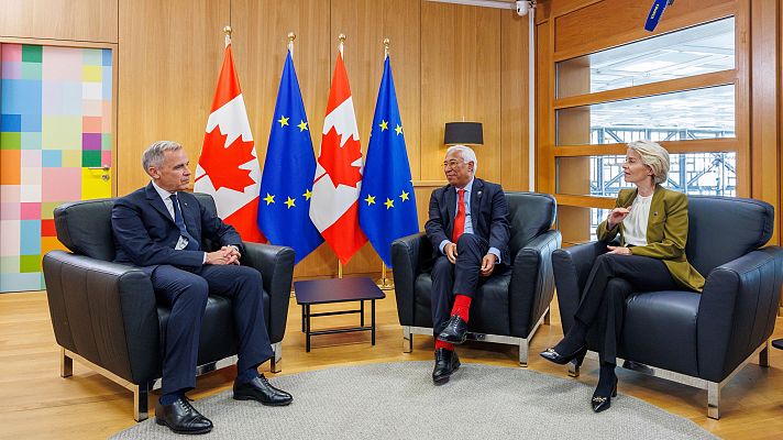 Ursula von der Leyen y António Costa conversan cordialmente junto a otro diplomático en una sala decorada con banderas de la Unión Europea y Canadá.