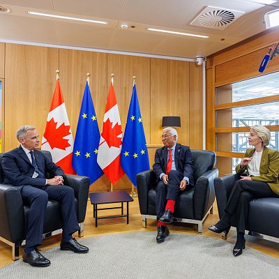Ursula von der Leyen y António Costa conversan cordialmente junto a otro diplomático en una sala decorada con banderas de la Unión Europea y Canadá.