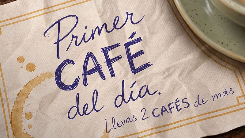 Servilleta de papel sobre una mesa de madera con el texto escrito a mano "Primer CAF� del d�a." y "Llevas 2 CAF�S de m�s", junto a una mancha de caf�.