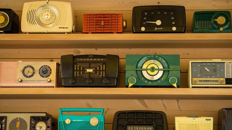 Colecci�n de radios vintage de marcas como RCA Victor, Zenith y Motorola, ordenadas en estanter�as de madera con variados dise�os, colores pastel y acabados de baquelita.
