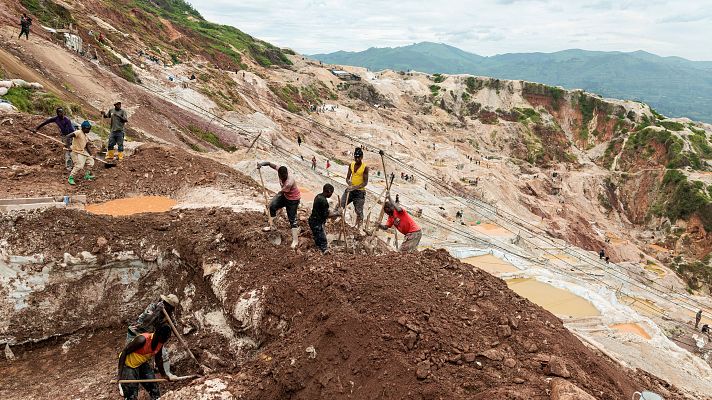 Mineros artesanales trabajan con palas en una enorme explotación a cielo abierto sobre un terreno arcilloso y erosionado en una zona montañosa de África.