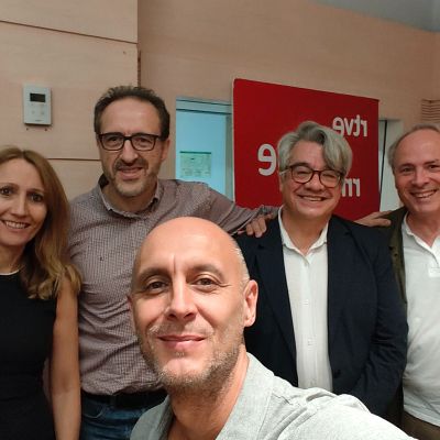 Paco Asensi se toma un selfi sonriente junto a cuatro acompañantes en un estudio de Radio Nacional de España (RNE), con el logotipo de la emisora visible al fondo.