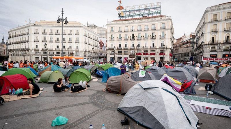 Acampada de protesta en la Puerta del Sol de Madrid con tiendas de campa�a, una pancarta de "HUELGA GENERAL" y el cartel de "T�o Pepe" al fondo bajo un cielo nublado.