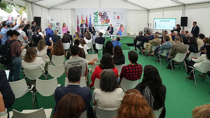 José Luis Martínez-Almeida inaugura el \"Día de las Profesiones\" en una carpa de moqueta verde ante un público donde destaca una camiseta con el texto \"TRABAJO SOCIAL MADRID\".